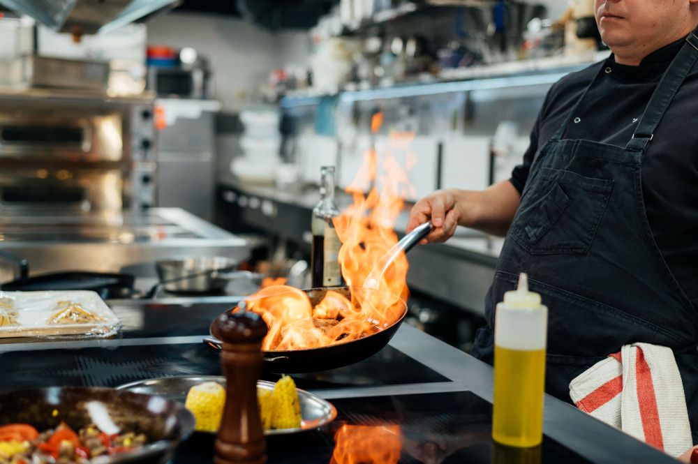 Seorang koki profesional sedang memasak di dapur restoran yang sibuk, gambaran efisiensi operasional yang didukung oleh sistem POS terintegrasi.
