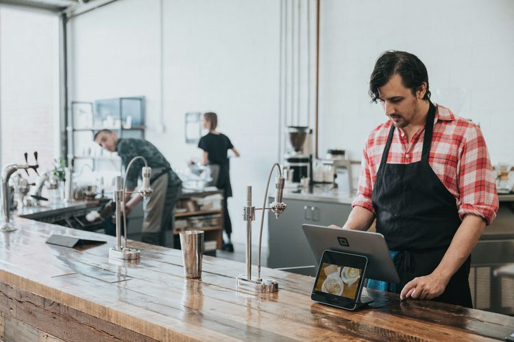 Suasana ramai coffee shop modern di Indonesia dengan barista menggunakan tablet POS ReBill untuk mencatat pesanan dan memantau transaksi real-time.